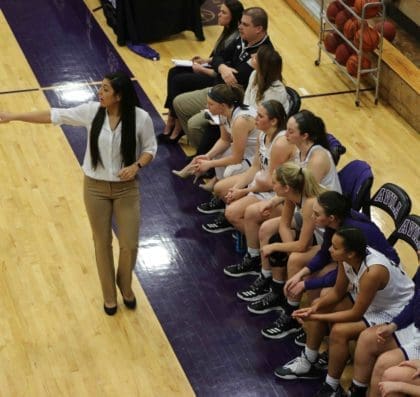 Overhead view of the Avila women's basketball team on the court side bench. Coach Murillo is calling out to players on the court