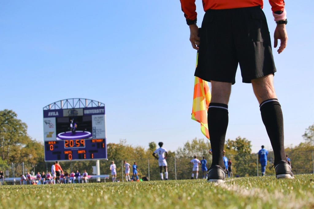 Ground level shot of a men's soccer match, the referee's legs are in the foreground