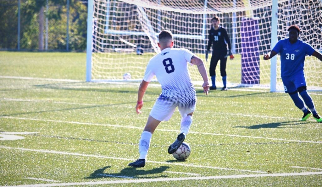 Avila men's soccer player dribbling before taking a shot on goal.