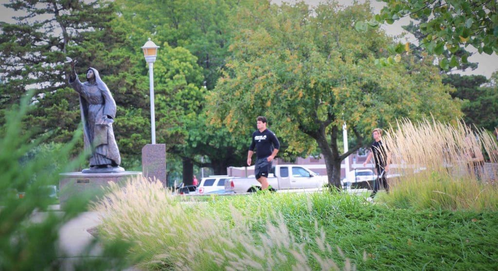 Two students walking toward statue of St. Teresa of Avila